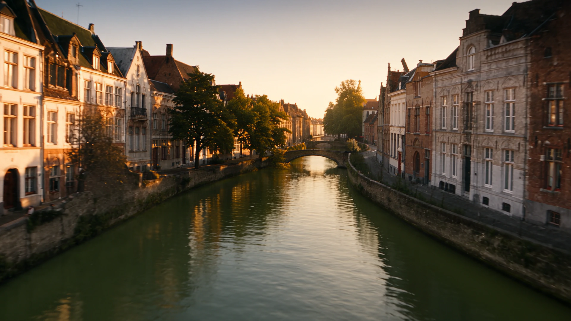 A Bruges canal at first light, with rows of houses standing on both banks and a bridge at the far end.