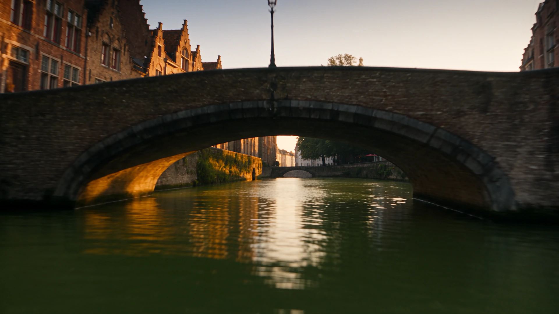 The underside of a stone bridge arch in Bruges, its curve doubled by the reflection in the water below.